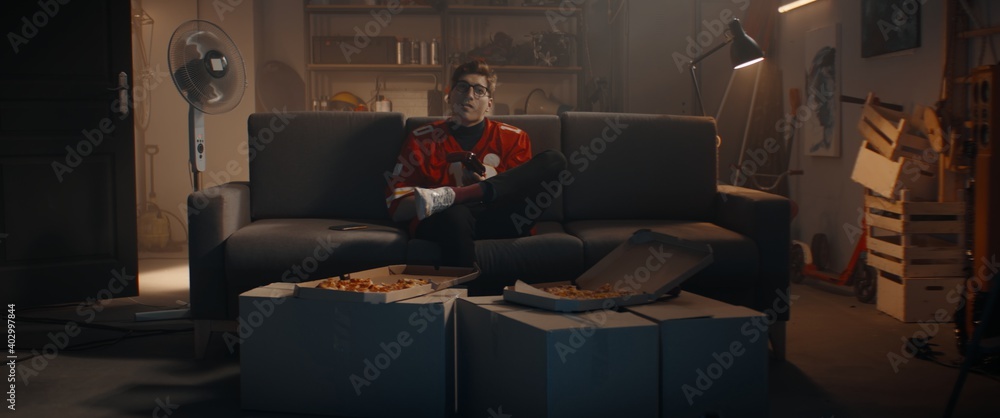 POV Portrait of Caucasian teenager playing video game inside home garage, enjoying pizza. Shot with 2x anamorphic lens - obrazy, fototapety, plakaty 