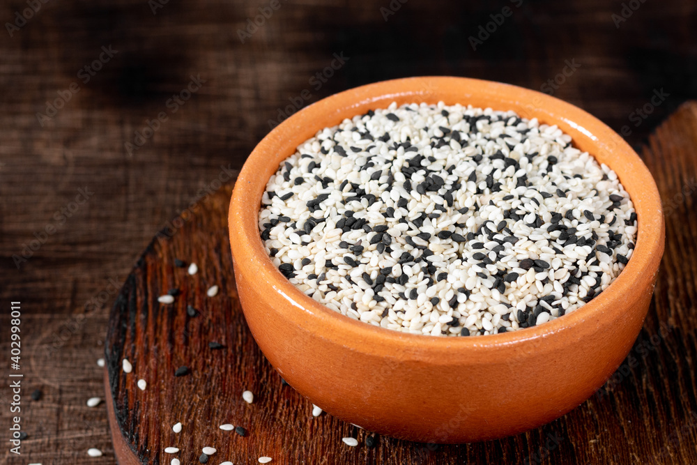 White and black sesame seeds in a ceramic bowl on a brown wooden table White and black sesame seeds in a ceramic bowl on a brown wooden table