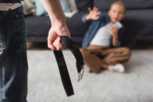 Man holding waist belt near kid on floor at home on blurred 