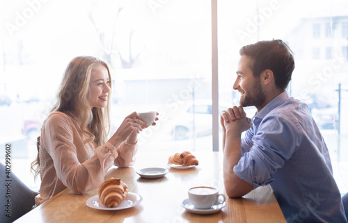 Affectionate young couple having brunch together at cafeteria, enjoying friendly talk near window, drinking coffee