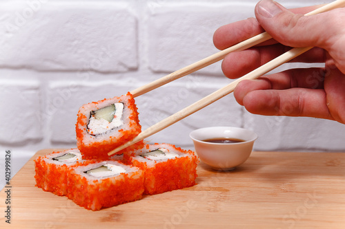 Man's hand holding chopsticks and eating sushi rolls on a wooden board