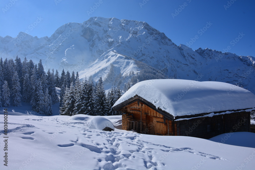 Winter landscape with wooden cabin covered with snow in the foreground and mountains covered with snow in the background