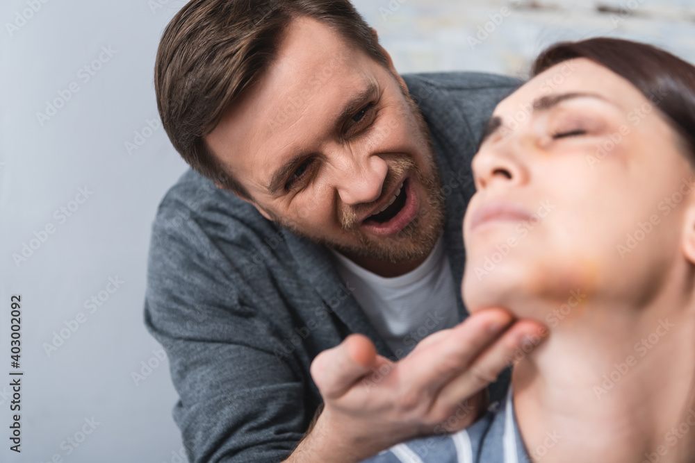 husband looking at wife with bruises on face on blurred foreground at home husband looking at wife with bruises on face on blurred foreground at home