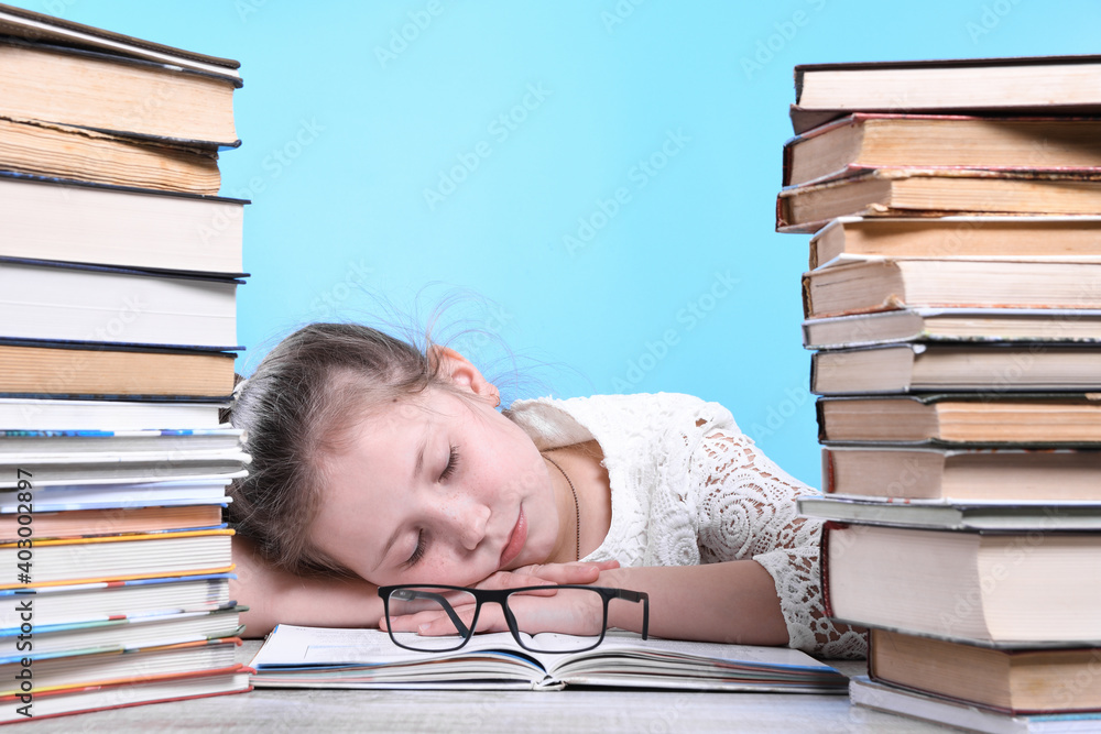 Back to school .Happy cute industrious child is sitting at a desk indoors. Kid is learning in class.Mountains of books on the sides Back to school .Happy cute industrious child is sitting at a desk indoors. Kid is learning in class.Mountains of books on the sides