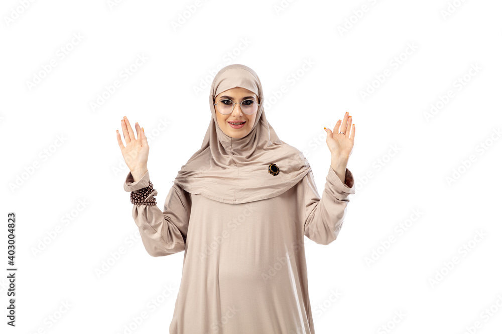 Showing. Beautiful arab woman posing in stylish hijab isolated on studio background with copyspace for ad. Fashion, beauty, style concept. Female model with trendy make up, manicure and accessories. Showing. Beautiful arab woman posing in stylish hijab isolated on studio background with copyspace for ad. Fashion, beauty, style concept. Female model with trendy make up, manicure and accessories.