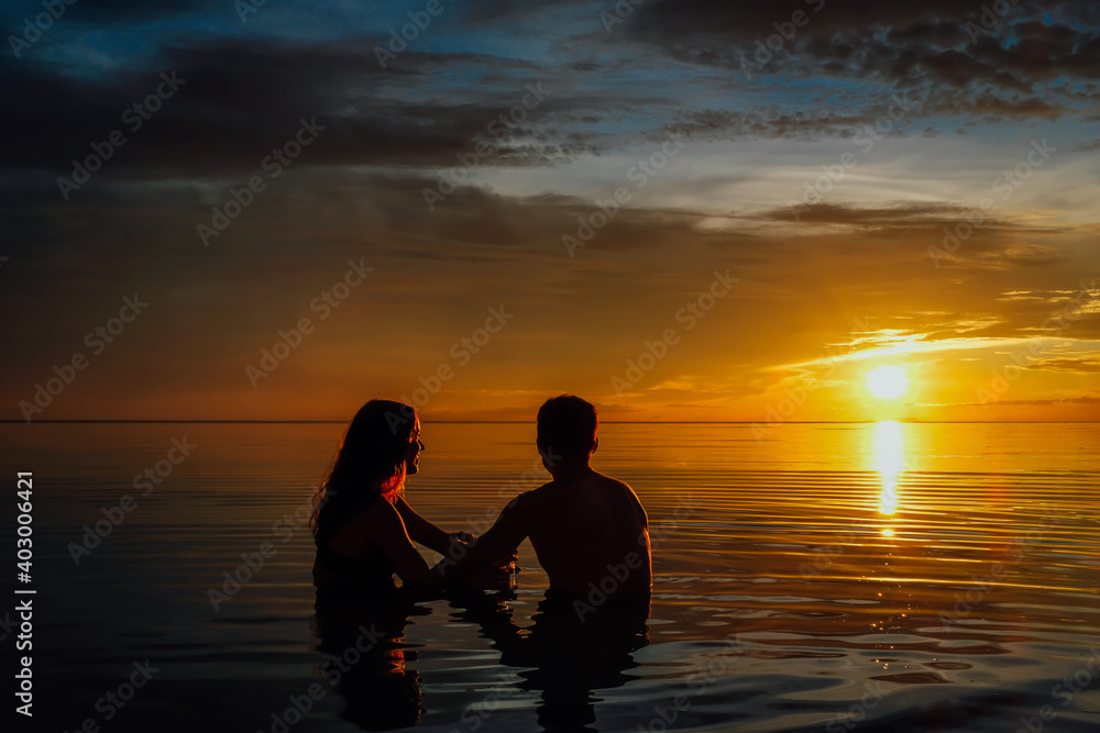 Young couple in the water watching a very colorful sunset on the beach