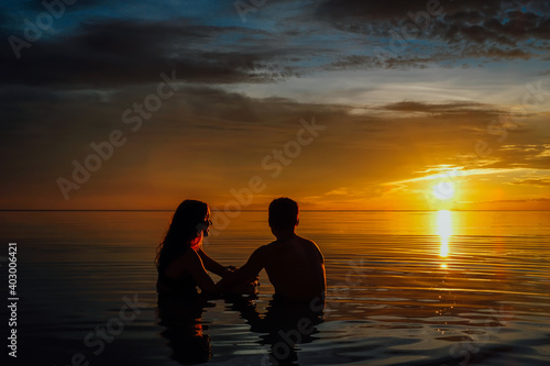 Young couple in the water watching a very colorful sunset on the beach