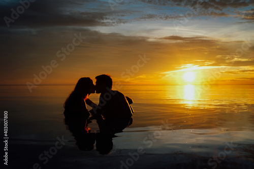 Young couple kissing and having a beer in the water during a very colorful sunset on the beach