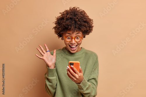 Foto Excited cheerful dark skinned curly young woman raises palm and stares overjoyed