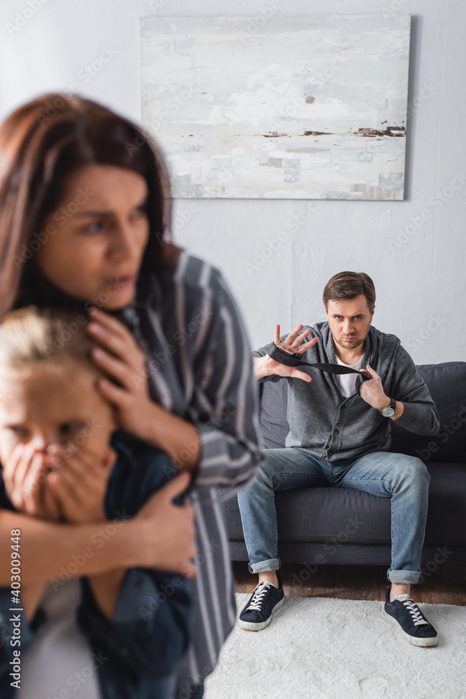 with waist belt looking at frightened wife hugging daughter on blurred foreground with waist belt looking at frightened wife hugging daughter on blurred foreground