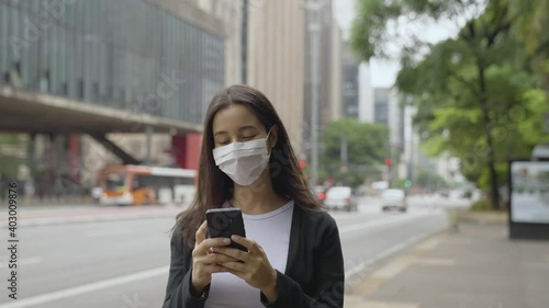  woman walking around paulista avenue wearing face mask using smartphone. Communication, social networks, online shopping concept.
 photo