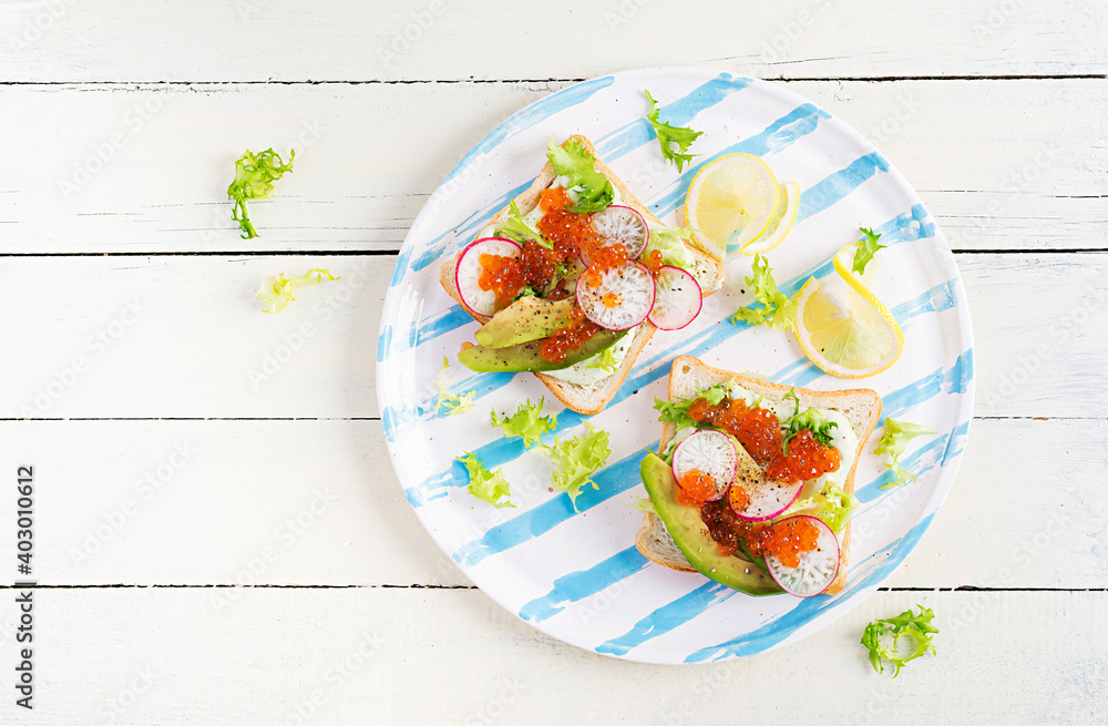 Sandwiches with salmon red caviar with sliced avocado and radish. Sandwich for lunch. Premium food. Overhead, top view, flat lay Sandwiches with salmon red caviar with sliced avocado and radish. Sandwich for lunch. Premium food. Overhead, top view, flat lay