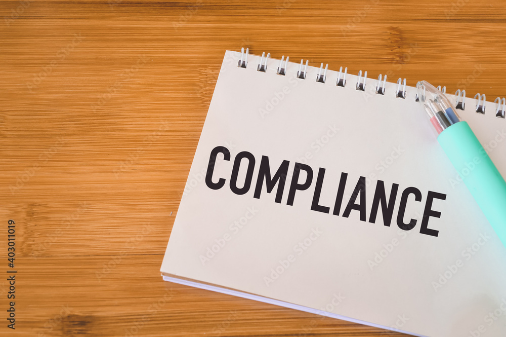 Top view of pen and notebook written with text COMPLIANCE. Top view of pen and notebook written with text COMPLIANCE.