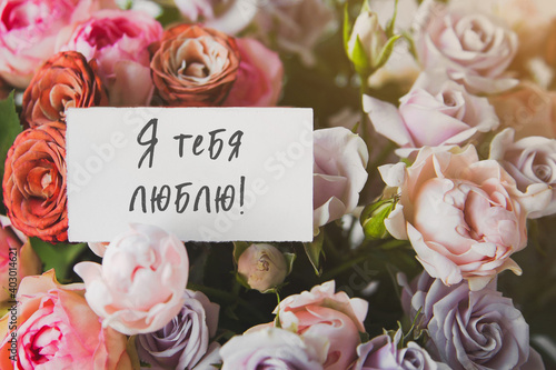 white gift card with the inscription I love you in Russian in a bouquet of bright beautiful multi-colored roses, the concept of congratulations on the holiday 