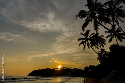 Fototapeta Naklejka Na Ścianę i Meble -  Blue sky at sunset on a beach with palm trees and horizon in silhouette