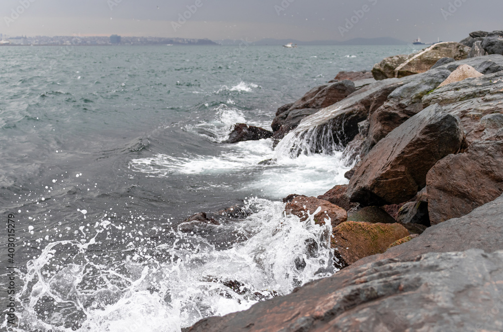 Landscape with sea waves crashing on huge stones, white sea foam and beautiful skyline.