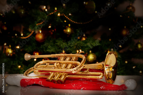 Obraz na płótnie Cornet – brass musical instrument – placed on Santa’s hat with a Christmas tree in the background. Festive holiday atmosphere with warm lights and musical charm. w salonie