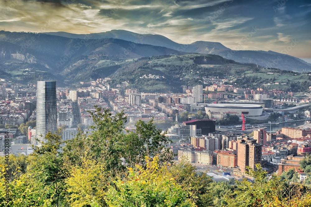 Vista general de la ciudad de Bilbao desde lo alto de una colina, con su estadio de futbol, rio, rascacielos y fondo de montañas.jpg