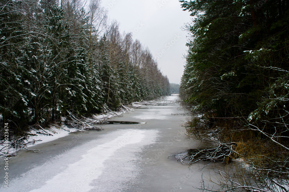 Winter forest river with snow-covered banks in the evening Winter forest river with snow-covered banks in the evening