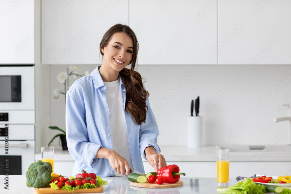 Young beautiful woman preparing a salad of fresh vegetables in a bright kitchen. Young beautiful woman preparing a salad of fresh vegetables in a bright kitchen.