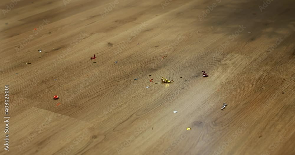 white automatic robot vacuum cleaner with brushes is cleaning confetti from wooden floor after christmas, birthday party. automatic cleaning of the apartment at a certain time. white automatic robot vacuum cleaner with brushes is cleaning confetti from wooden floor after christmas, birthday party. automatic cleaning of the apartment at a certain time.