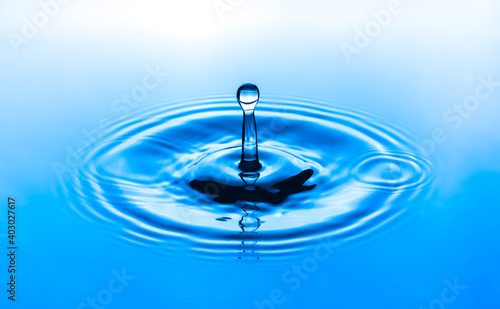 Water drop splashing into blue water surface. Health and purity concept