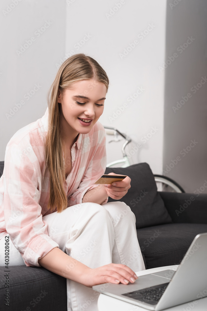 happy young woman holding credit card and using laptop on coffee table happy young woman holding credit card and using laptop on coffee table