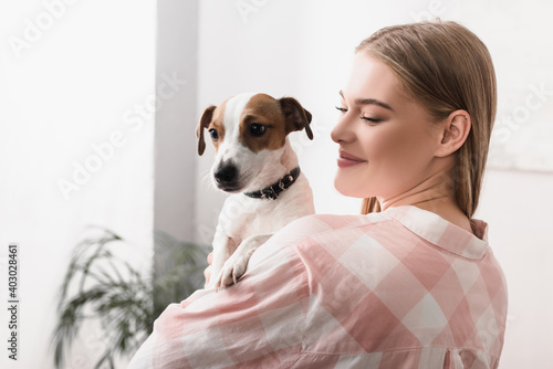young cheerful woman holding in arms jack russell terrier in living room