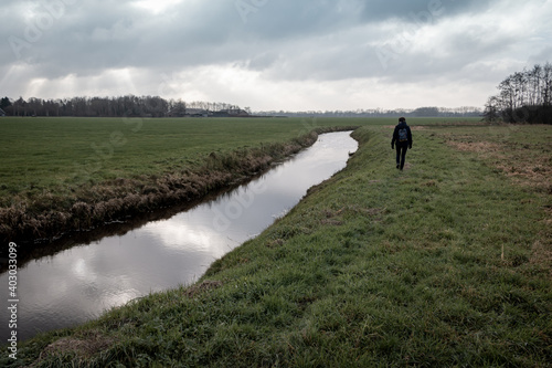 Lonely hiker in a wintry Dutch landscape with grasslands, ditches and threatening dark skies