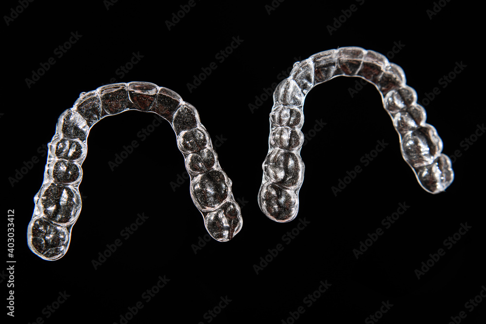Invisible dental teeth brackets tooth aligners on black background. Plastic braces dentistry retainers to straighten teeth. Invisible dental teeth brackets tooth aligners on black background. Plastic braces dentistry retainers to straighten teeth.