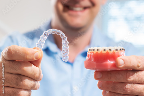 Dental care.Smiling orthodontist doctor holding aligners and braces in hand shows the difference between them