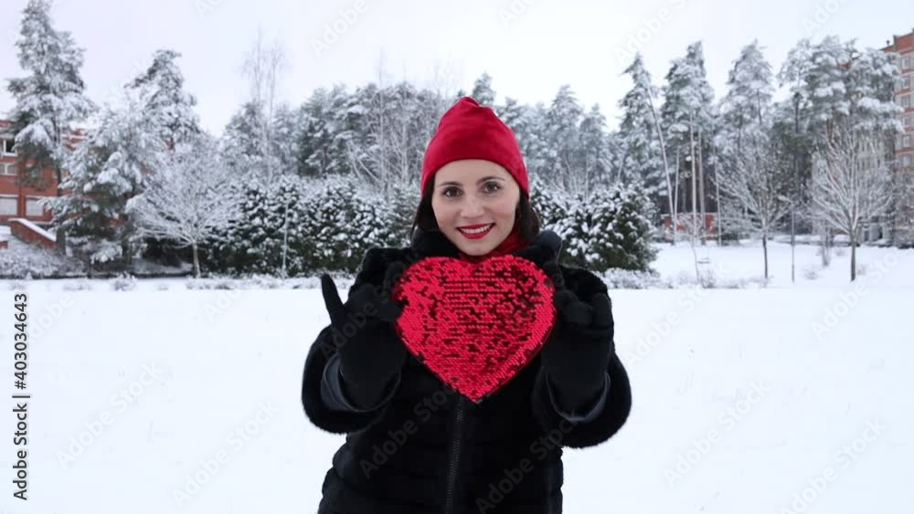 Young romantic woman in red hat touches heart with sequins. Snow outside. Winter time. Love and leisure concept. Valentines day. Love Young romantic woman in red hat touches heart with sequins. Snow outside. Winter time. Love and leisure concept. Valentines day. Love