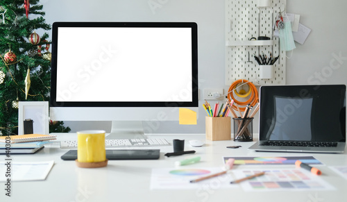 Creative designer workspace with blank screen computer, laptop, colourful paper charts and assessories on white table photo