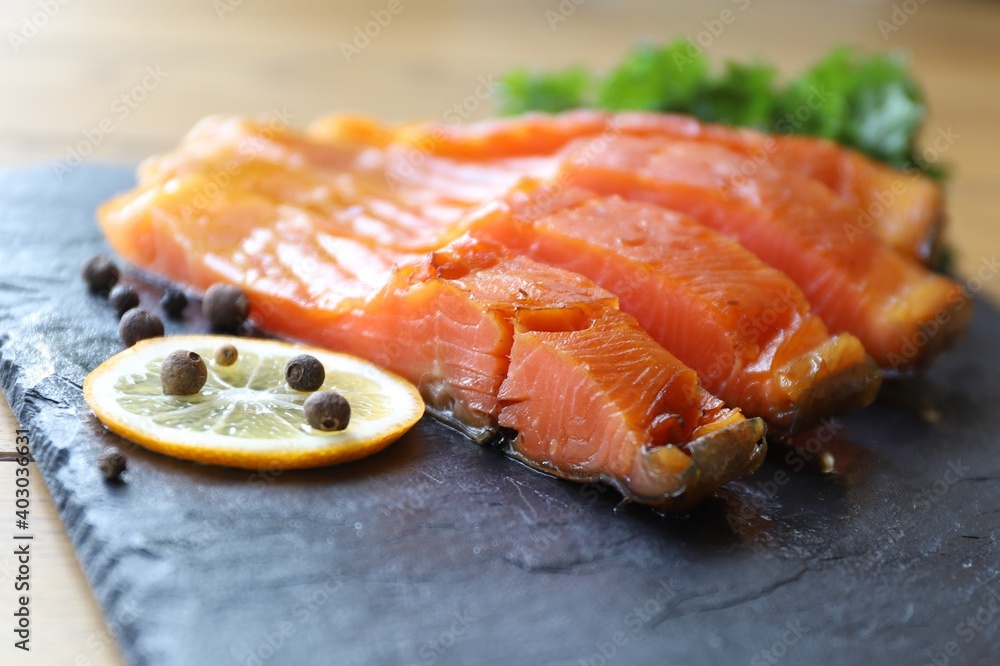 pieces of sea trout lie on a black basalt platter next to lemon slices spices and herbs pieces of sea trout lie on a black basalt platter next to lemon slices spices and herbs