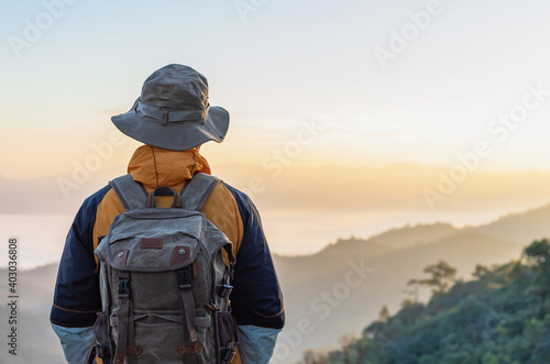 Hipster male hiker with backpack enjoying sunset on peak of foggy mountain. Tourist traveler on background view mockup.