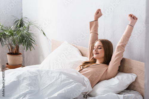 Фотография awake and joyful woman in satin pajamas stretching in bed