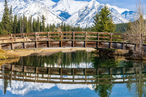 Wooden arch footbridge in Cascade Ponds park in autumn sunny day, snow-covered Mount Astley reflection on the water surface. Banff National Park, Canadian Rockies, Alberta, Canada. photo