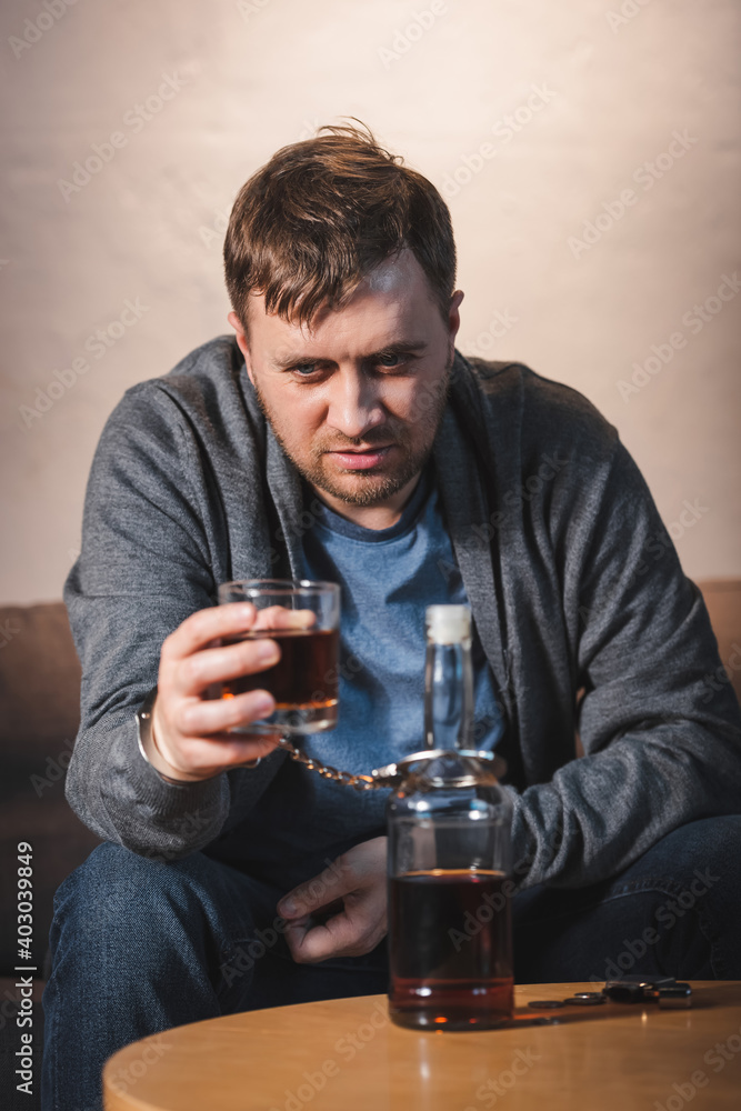 drunk man, handcuffed to bottle of alcohol, holding glass of whiskey, blurred foreground drunk man, handcuffed to bottle of alcohol, holding glass of whiskey, blurred foreground