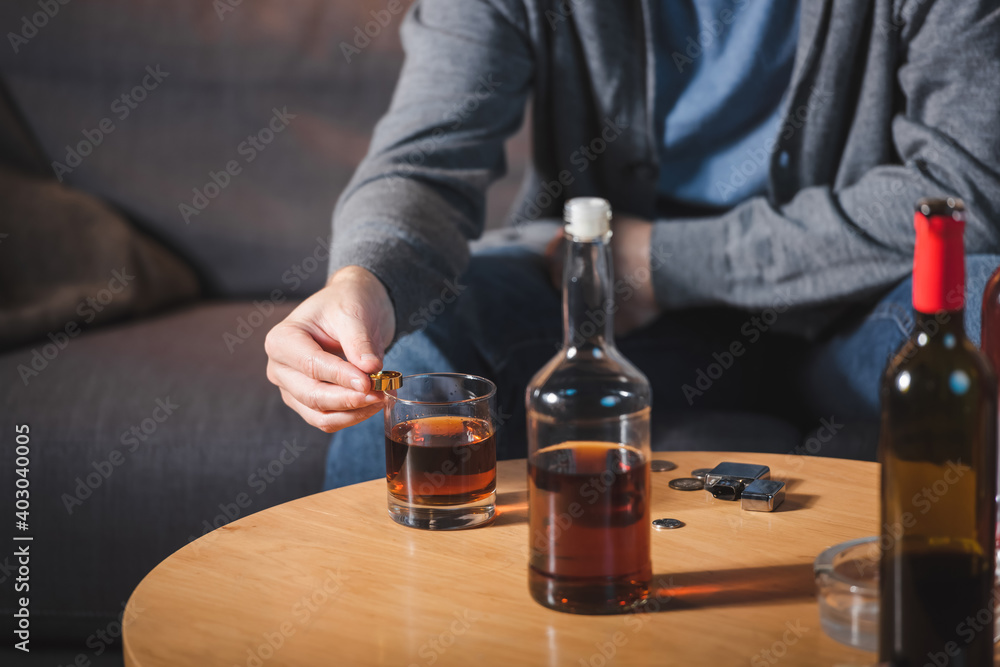 cropped view of man holding wedding ring near glass and bottle of whiskey, blurred background