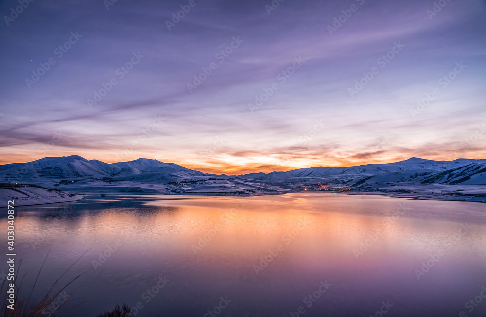 Beautiful winter landscape. Panoramic view on the lake  and mountains peaks snow-covered after sunset. 