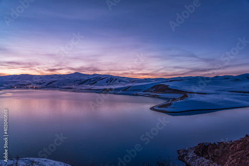 Beautiful winter landscape. Panoramic view on the lake and mountains peaks snow-covered after sunset. 
