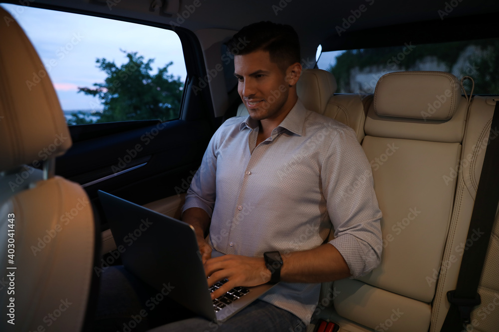 Handsome man working with laptop on backseat of modern car Handsome man working with laptop on backseat of modern car