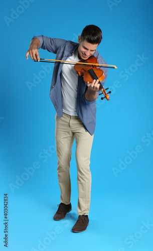 Happy man playing violin on light blue background