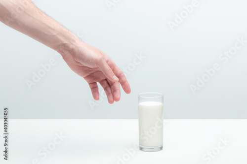 Man prepearing to take a glass of milk. Hand reaching for a full transparent glass on a table. Finger not touching the edge of a glass.