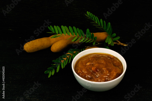 Tamarind juice in white bowl and tamarind fresh tropical fruit with leaf on black wooden background for cooking, dark tone. photo