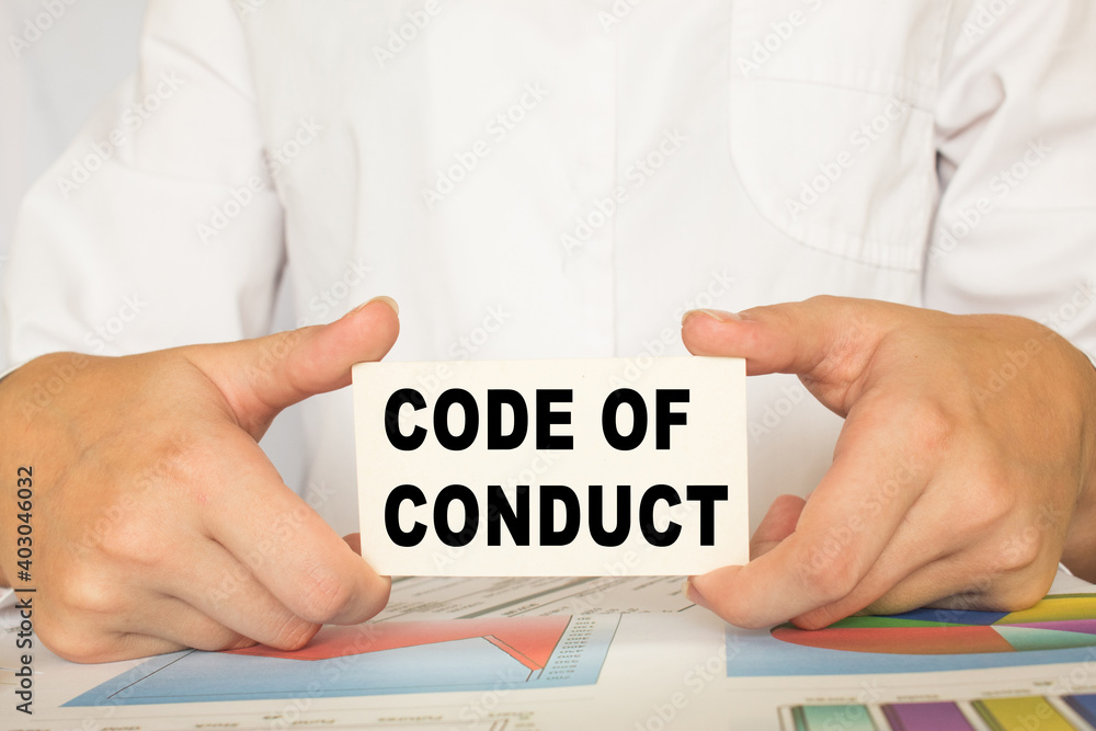 a man in the office holds a card with text CODE OF CONDUCT. business concept a man in the office holds a card with text CODE OF CONDUCT. business concept