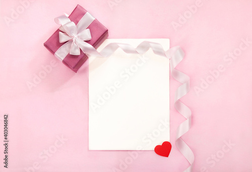 Valentines day greeting card with pink gift box, white bow, long curved ribbon and paper red heart. Tope view, empty space for text © Aivolie
