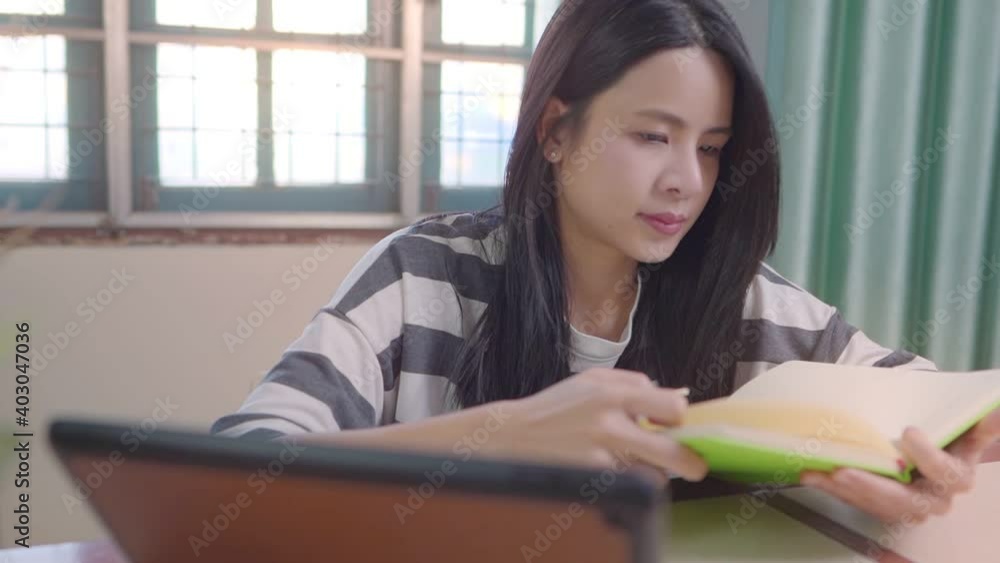 Young asia girl reading book at home table with tablet on the side, focusing concentrating on study, college student reviewing for exam test, self discipline general knowledge, free time leisure Young asia girl reading book at home table with tablet on the side, focusing concentrating on study, college student reviewing for exam test, self discipline general knowledge, free time leisure