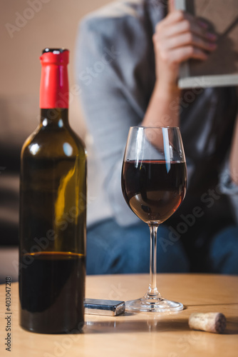 glass and bottle of red wine near alcohol-addicted woman on blurred background