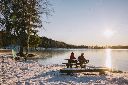 Two people sitting by the wooden table in the nature during winter time on a sunny day at Sognsvann lake in Oslo, Norway photo